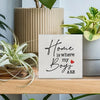 A rustic wooden sign with black script that reads Home is where my boys are with a small red heart, displayed on a light wood