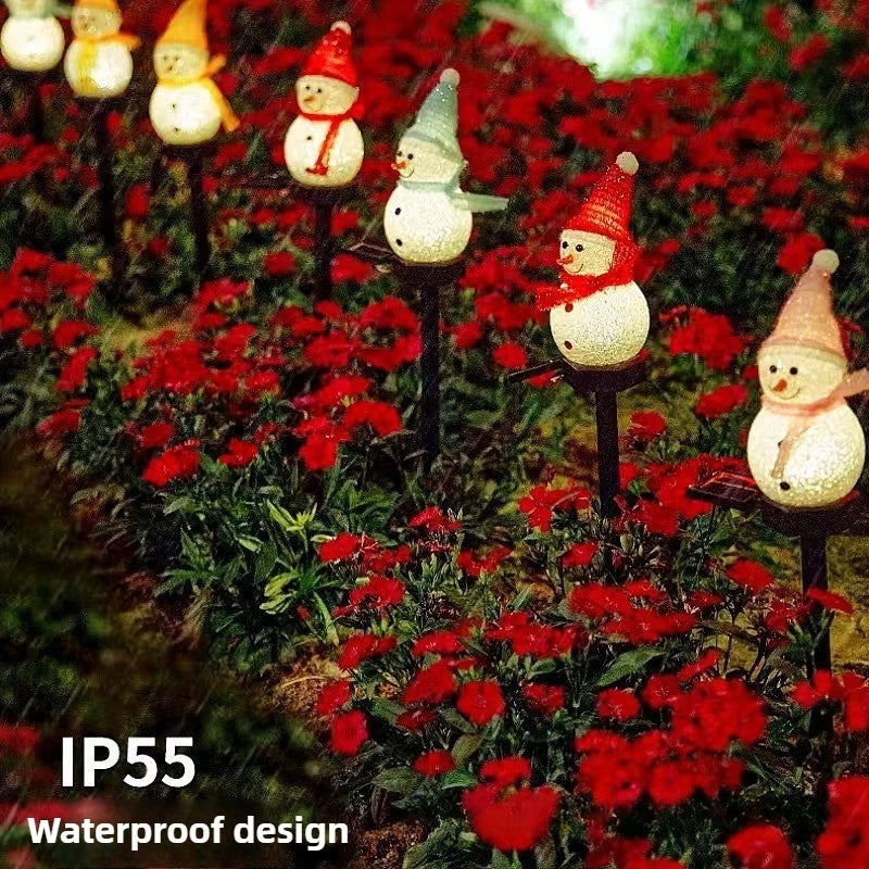 Red flowers surround small snowman lights planted in the ground