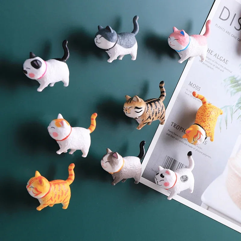 A collection of 3D cartoon cat refrigerator magnets in various colors and styles displayed on a green surface.