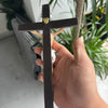 A hand holds a dark wood crucifix with a gold-colored finial against a blurred green plant background.