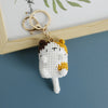 A handcrafted crochet cat keychain pendant with white and yellow yarn, attached to a gold-colored keyring.