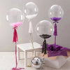 A display of transparent inflatable bobo balloons in various colors, including pink, purple, and black, on a white table.