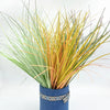A bundle of artificial grass greenery with variegated green and yellow blades in a blue pot.