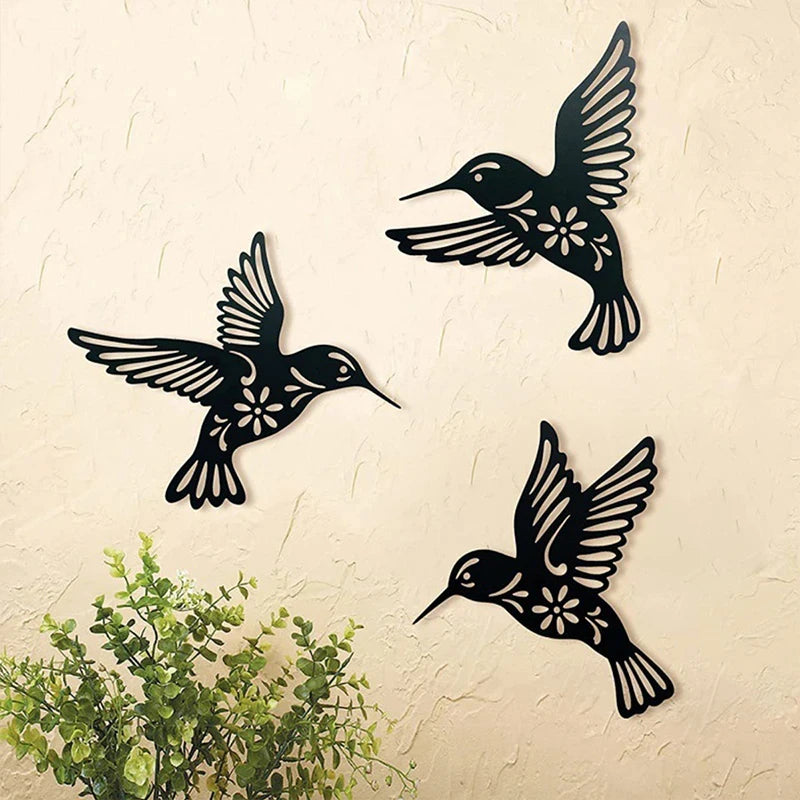 A set of three black metal hummingbird wall decor silhouettes on a beige wall.