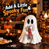 A white ghost figurine holding a soda can sits on a dark wooden table surrounded by Halloween decor.