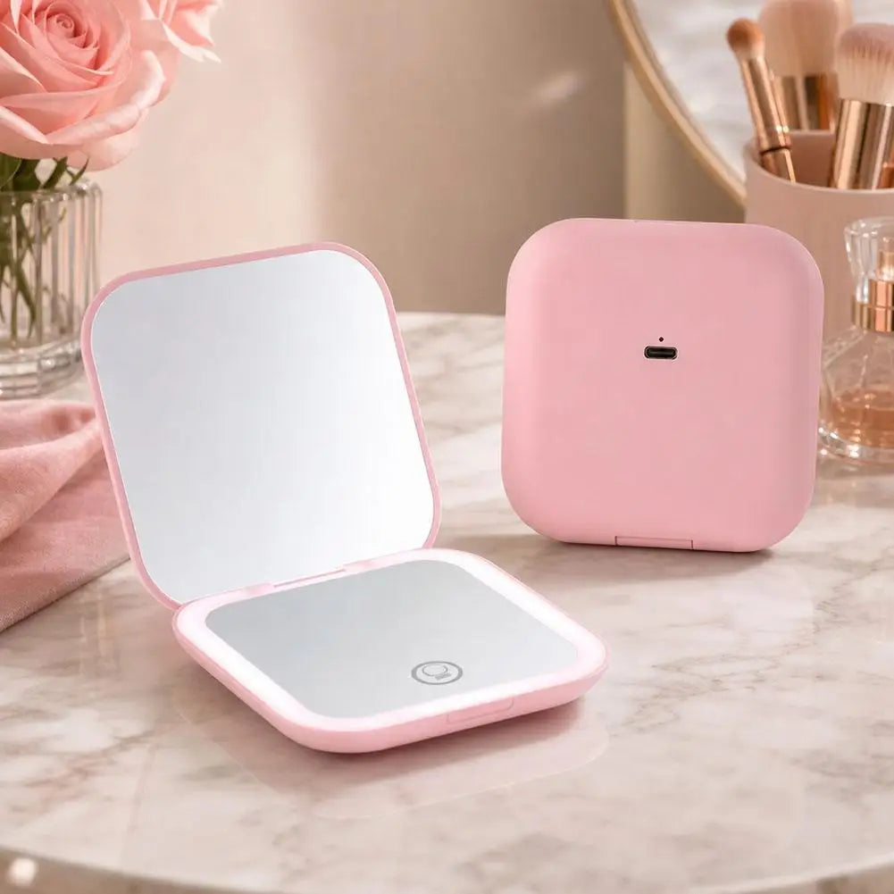 A pink portable folding LED makeup mirror with a reflective surface and a separate magnifying base is displayed on a marble t