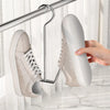 A hand is hanging a light beige shoe onto a stainless steel hanger.