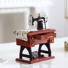 A miniature retro sewing machine music box with a dark body and silver accents sits on a wooden base.
