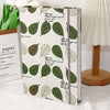 Un álbum de scrapbooking con funda de gran capacidad y hojas verdes, junto a una lámpara blanca.