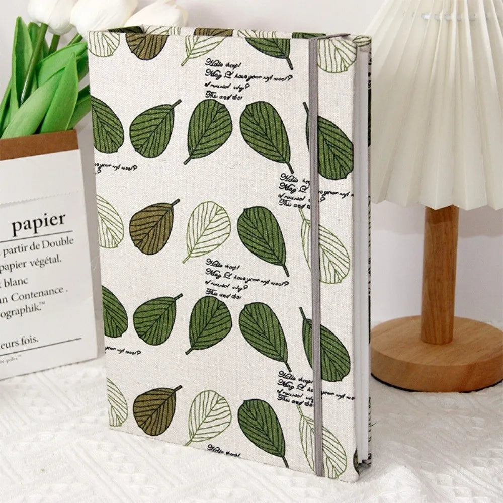 Un álbum de scrapbooking con funda de gran capacidad y hojas verdes, junto a una lámpara blanca.