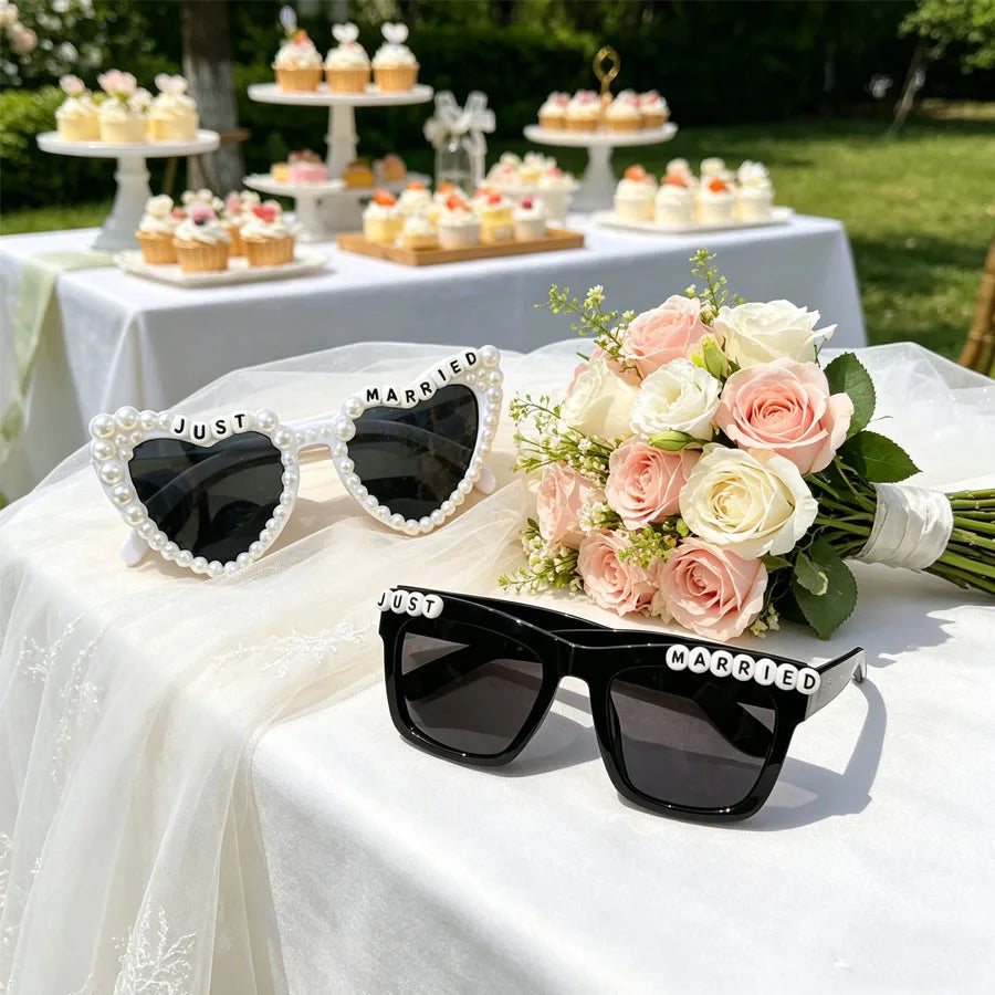 A set of black sunglasses with pearl detailing labeled Just Married displayed on a white tablecloth.