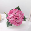 A cluster of pink artificial hydrangea flowers on green leaves.