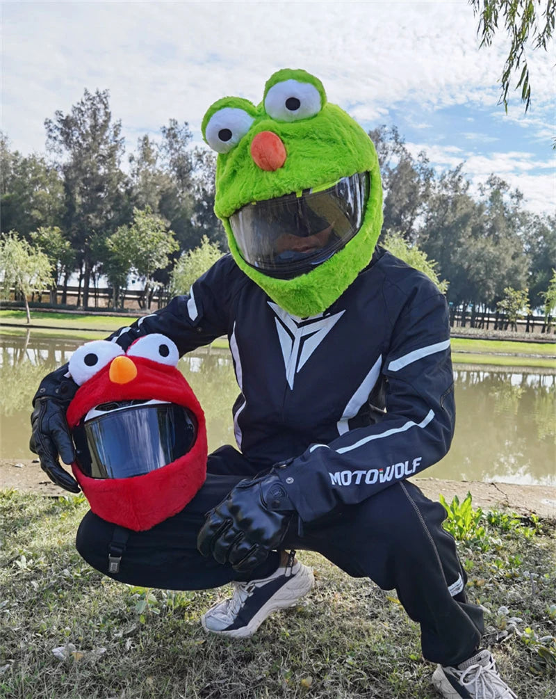 A green cartoon plush helmet cover with large eyes is shown outdoors.