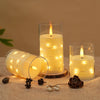 A glass candle holder with a glowing yellow LED star string candle and a lit taper candle on a wooden surface.
