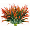 A vibrant artificial tall grass and tropical flower arrangement featuring spiky leaves in shades of red, orange, and green.