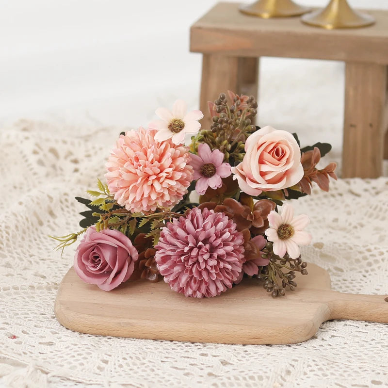 A bouquet of pink and peach silk roses and hydrangea flowers arranged on a wooden board.