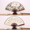 A retro folding silk and bamboo decorative fan with a light beige and gray landscape design displayed on a wooden surface.