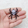 Un colgante de araña de acrílico negro con diseño de calavera sostenido en la mano de una persona.