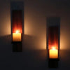 Two vintage wooden wall candle holders with glowing candles mounted on a dark wall.