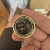A hand holds a gold-colored collectible coin featuring an alligator and the text Make America Safe Again.