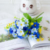 A bouquet of blue and white artificial daisy flowers displayed on an open book with a cute ceramic mug in the background.