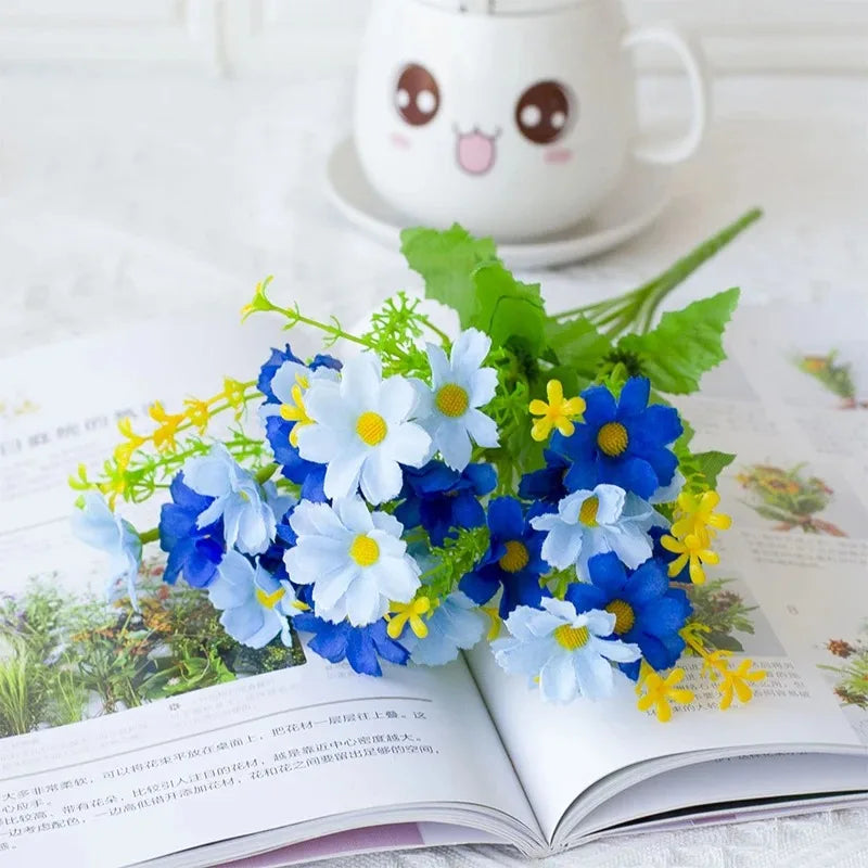 A bouquet of blue and white artificial daisy flowers displayed on an open book with a cute ceramic mug in the background.