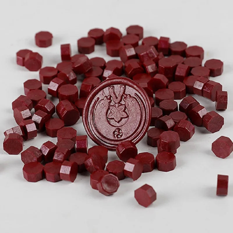 A pile of deep red wax sealing beads in various sizes and shapes for custom stamps.