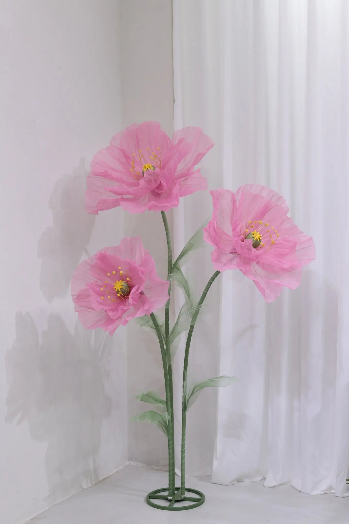 Large artificial silk pink poppy flowers displayed on a green stand against a white background.