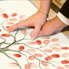 Une main applique des empreintes roses et rouges sur une impression de toile représentant une structure d'arbre.