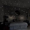 A bedroom wall decorated with glow-in-the-dark star stickers and a moon, illuminating a bed.