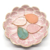 A pink scalloped dish holds three oval pendant charms made of rose quartz and natural agate stones.