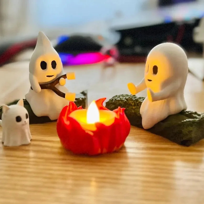 A set of white ghost figures and a red candle arranged on a wooden surface.