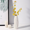 A white vase holds a tall spray of yellow wildflowers against a light background.