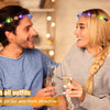 A smiling couple wearing glowing flower wreath headbands while looking at each other.