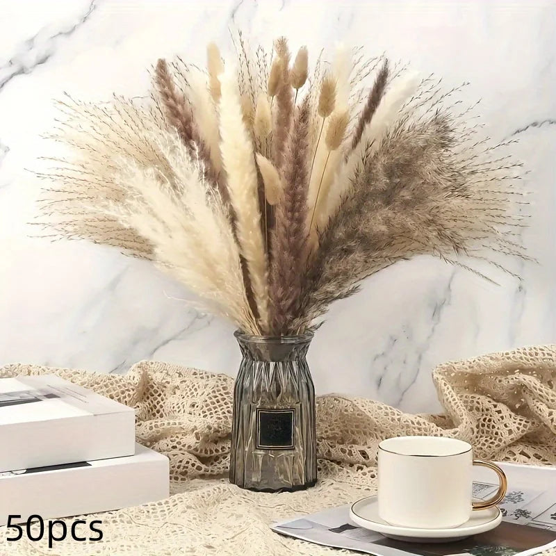 A dried flower bouquet of pampas grass in a silver vase resting on a beige textured fabric.