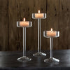 Three tall glass candle holders with lit candles on a dark wooden surface.