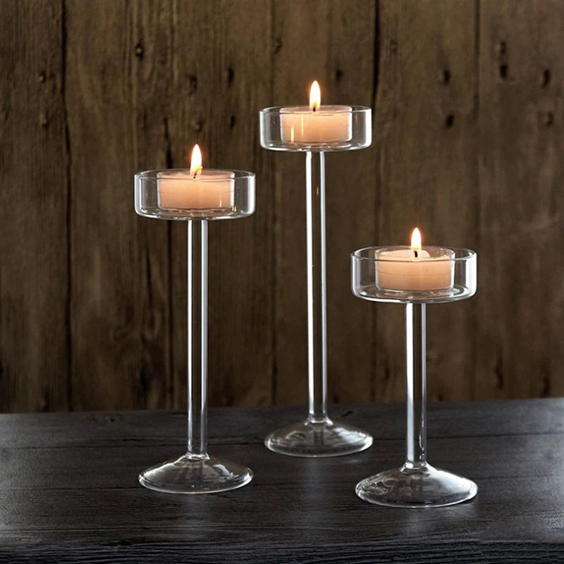 Three tall glass candle holders with lit candles on a dark wooden surface.