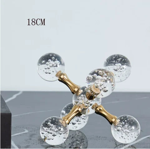 A minimalist molecular sculpture desk decor featuring gold-toned glass spheres with bubbles on a clear stand.