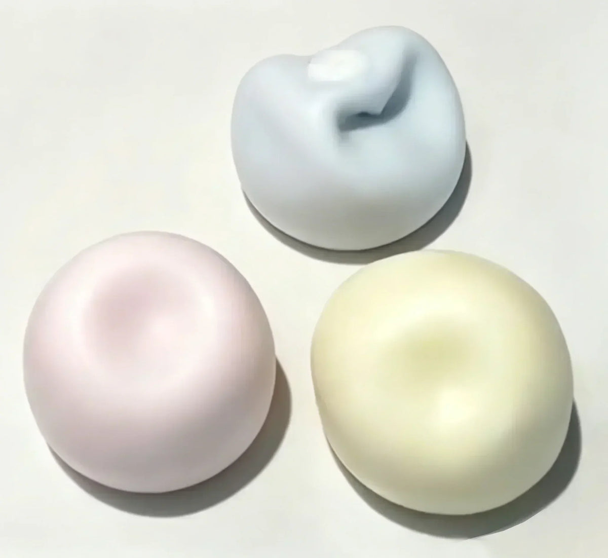 Three squishy toys shaped like cat paws in pastel colors pink blue and yellow