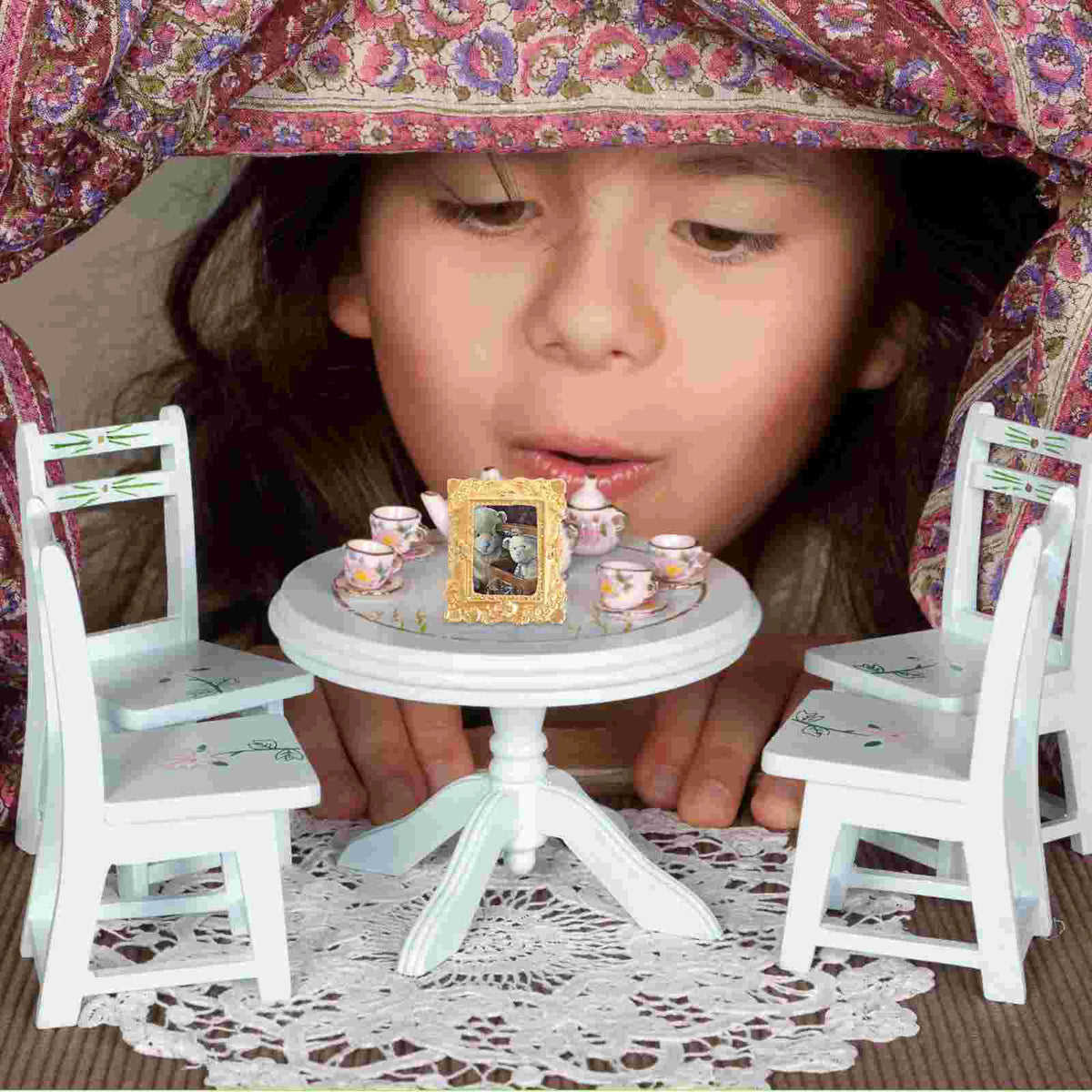 A young girl is holding a vintage gold oval miniature photo frame in front of a lace tablecloth.