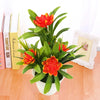 Artificial lotus flowers in bright orange and red bloom from green leaves displayed in a white pot.