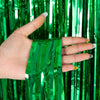 A hand holds a vertical green metallic foil fringe curtain backdrop.