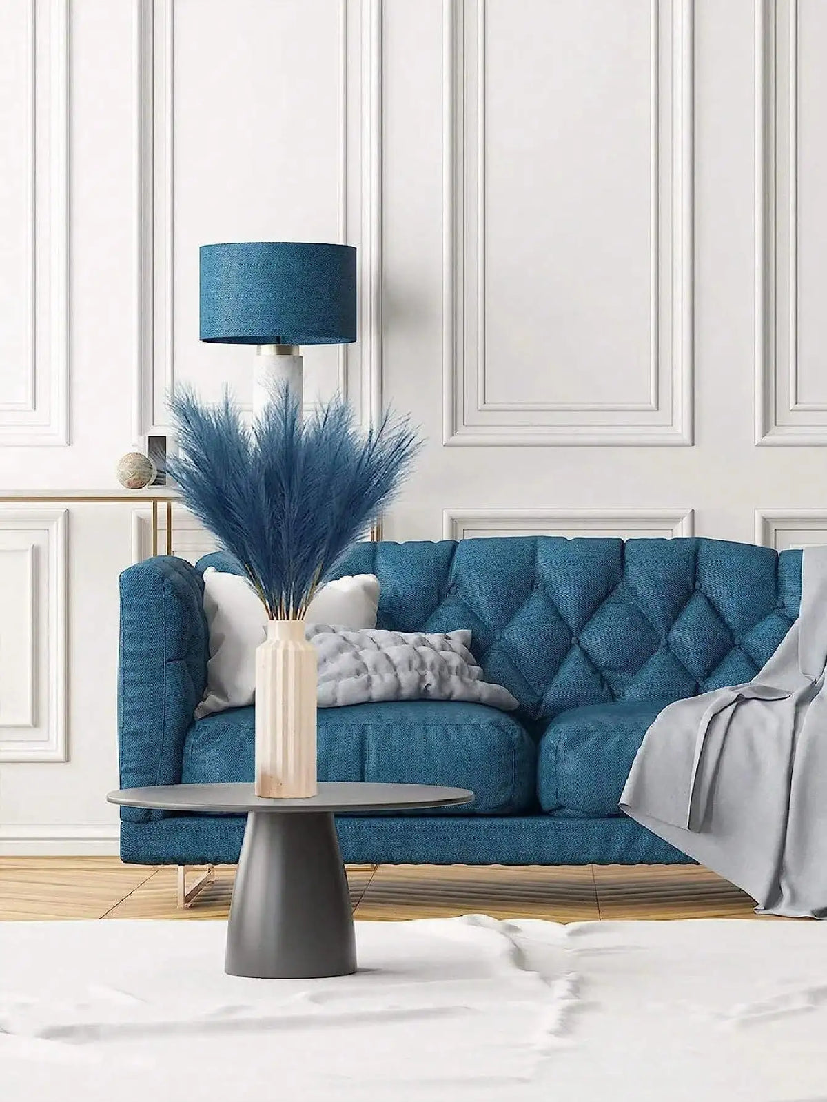 A teal lamp with a blue shade sits on a sofa, decorated with artificial pampas grass stems.