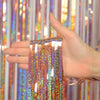 A hand holds a set of metallic foil tinsel fringe strands against a colorful curtain backdrop.