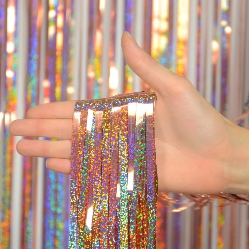 A hand holds a set of metallic foil tinsel fringe strands against a colorful curtain backdrop.