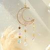 A golden crescent moon dreamcatcher featuring a pink quartz disc and dangling iridescent crystals.