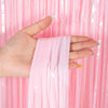A hand is holding a pink metallic tinsel foil fringe curtain backdrop for parties.