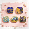 A set of five enamel pins featuring Van Gogh's art, including Starry Night and other classic paintings, displayed on pink pap