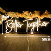 A glowing neon sign spelling Better Together is displayed against a dark background with floral decorations.