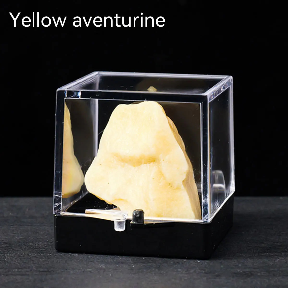 A yellow aventurine crystal specimen is displayed inside a clear box on a dark surface.